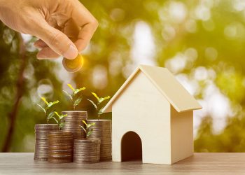 Property investment or saving money for buy home. Property investment or saving money for buy home. A businessman hand holding coin over growing plant on stacked coins and resident house model on wooden table.